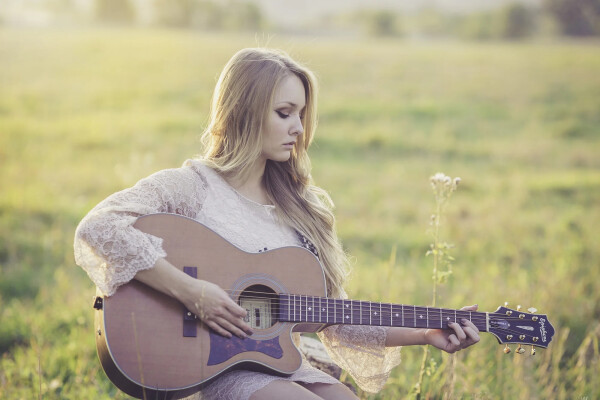 Uitvaart muziek, meisje dat gitaar speelt in de natuur bij ondergaande zon